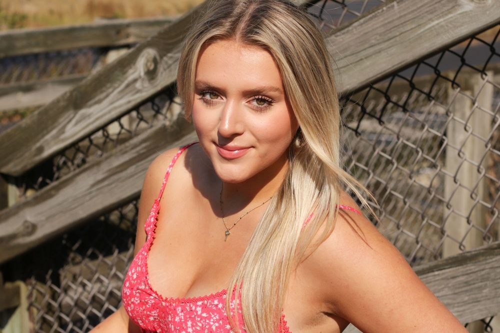 Person in pink top posing near wooden beach walkway with ocean view.