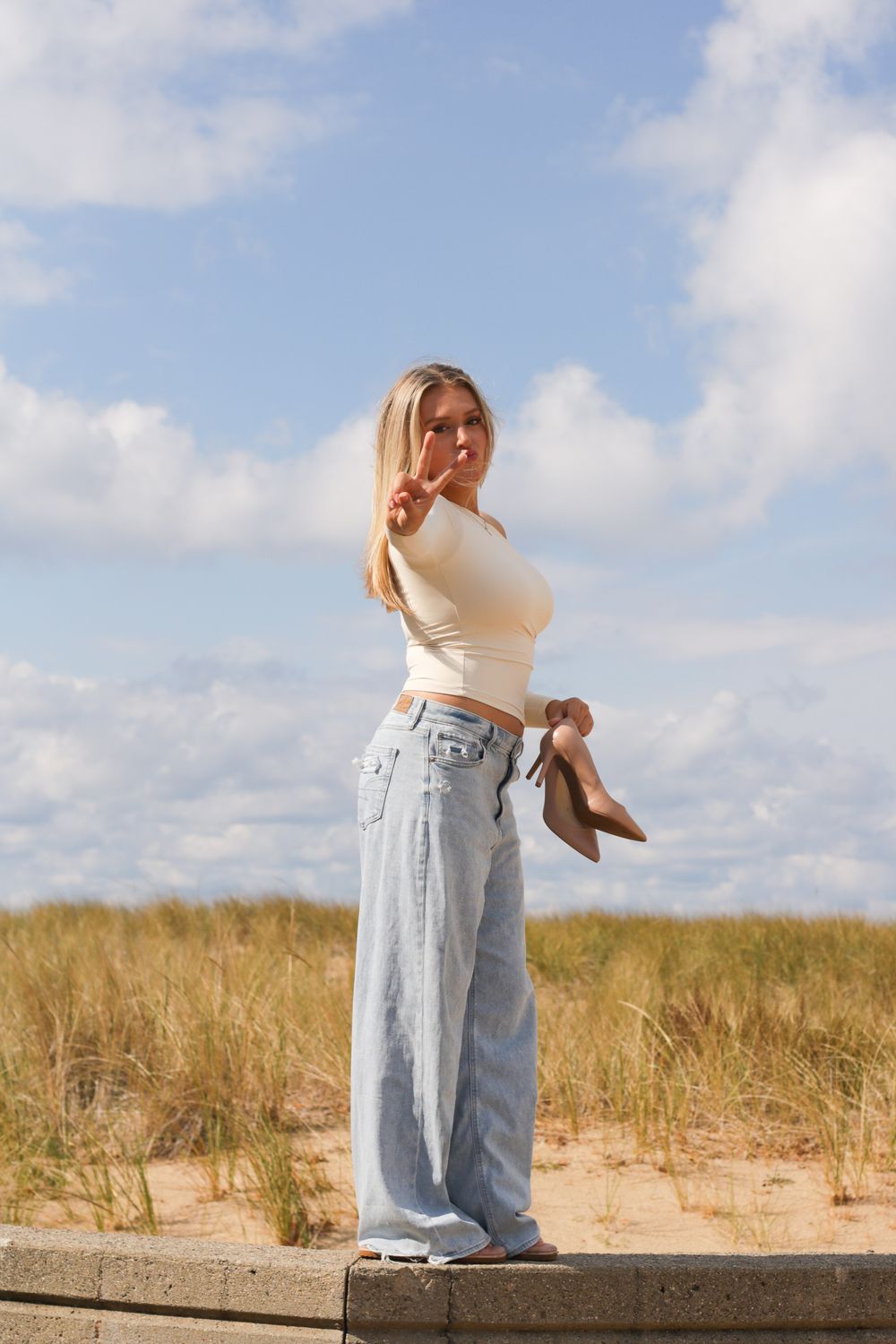 Person in light denim and white top posing on wooden walkway with beach grass.