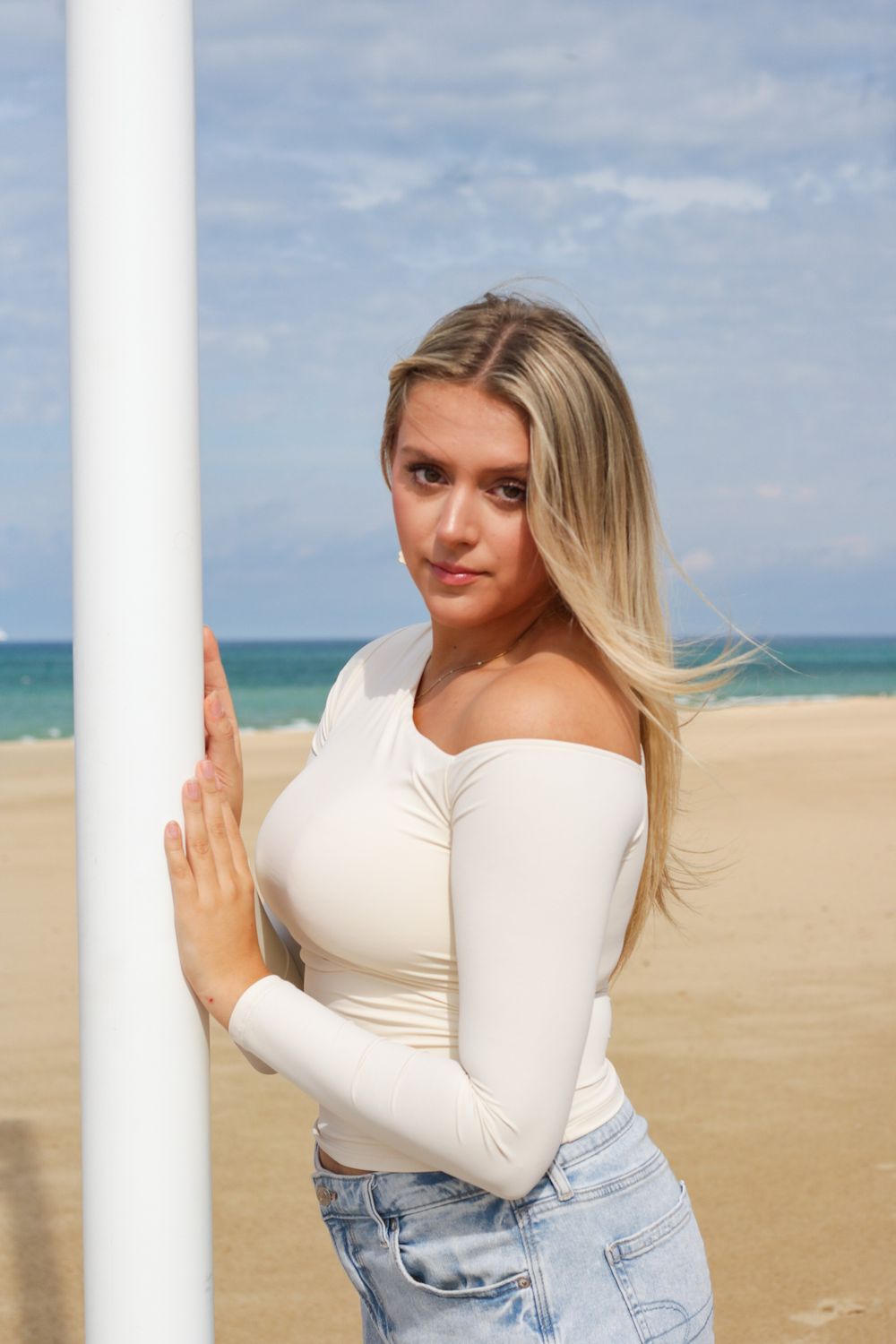 White long sleeve top and light denim jeans photographed against a beachy coastal backdrop.