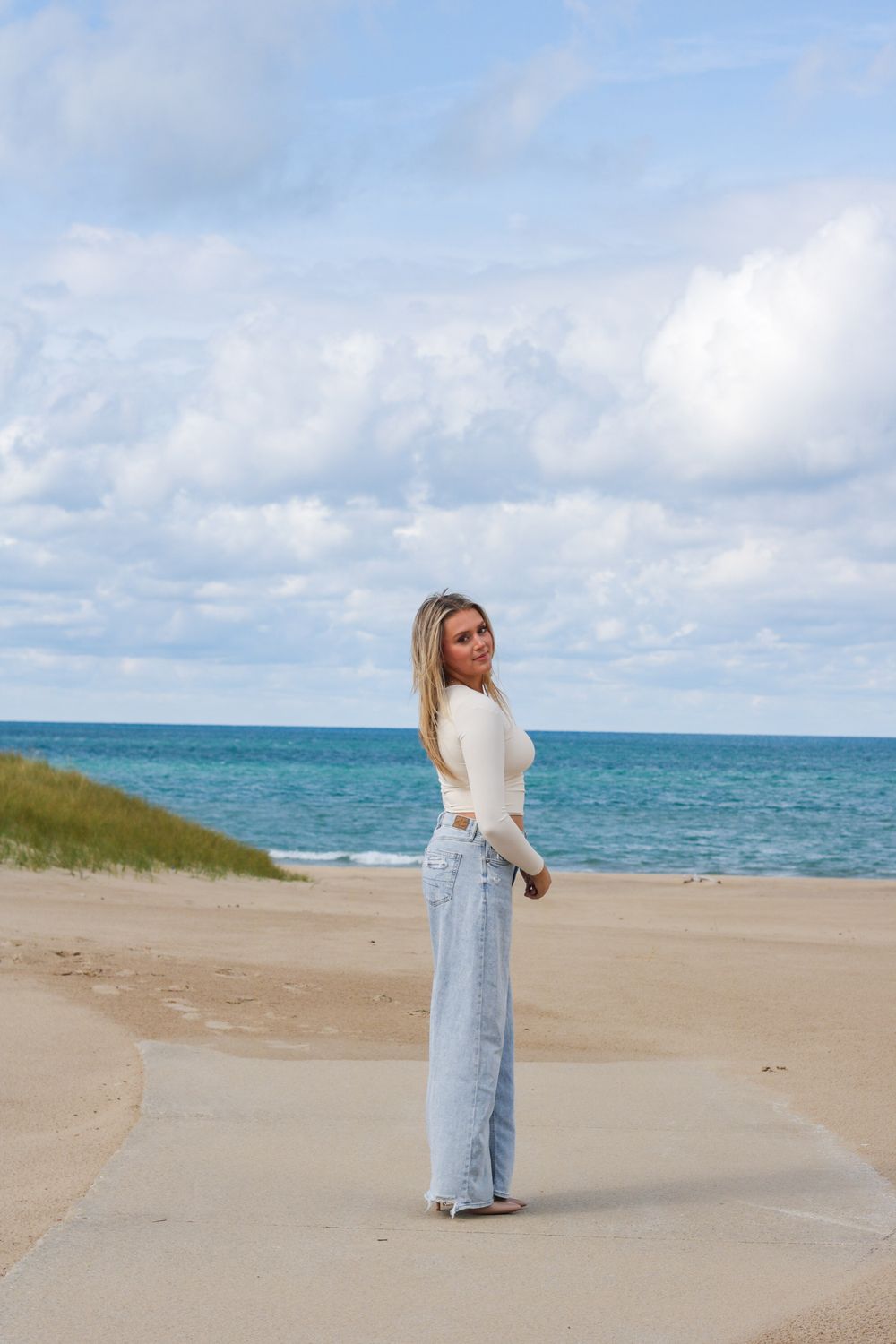 A sandy beach setting with bright turquoise water and beige sand dunes under a cloudy sky.