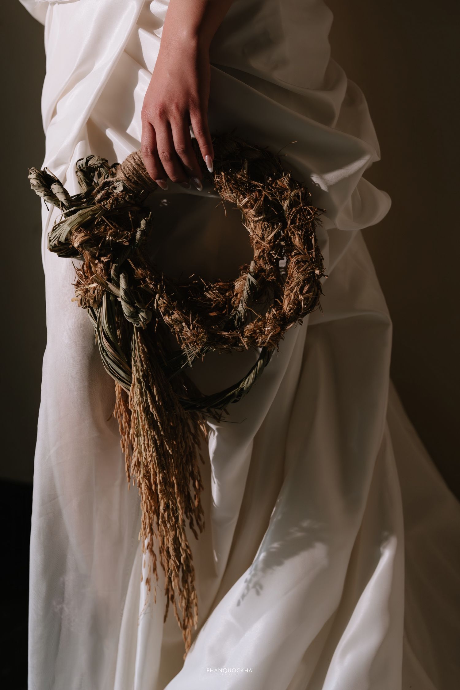 Close-up of bride holding rustic dried wreath bouquet against white wedding dress.