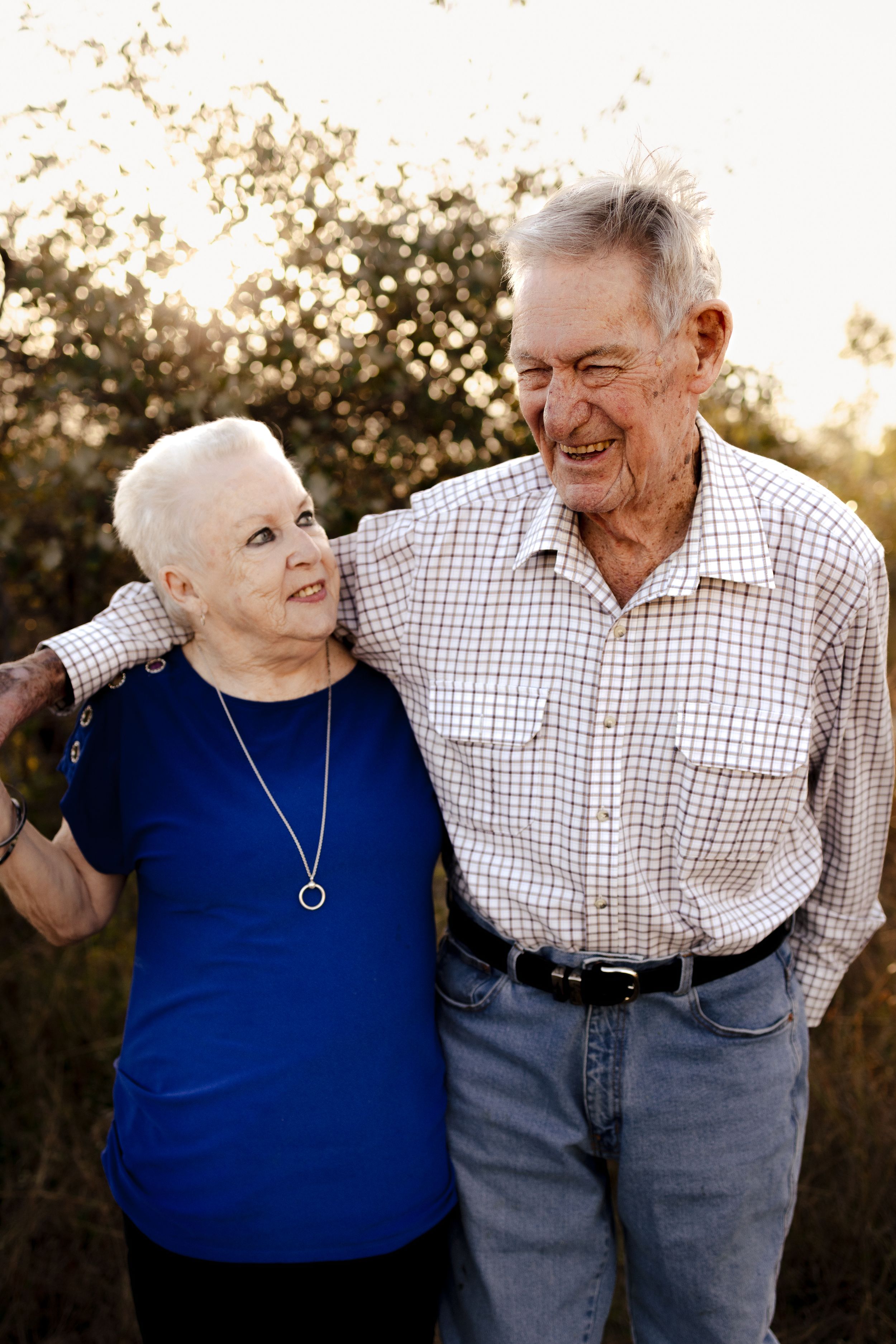 Elderly couple sharing a joyful moment outdoors in casual attire during golden hour.