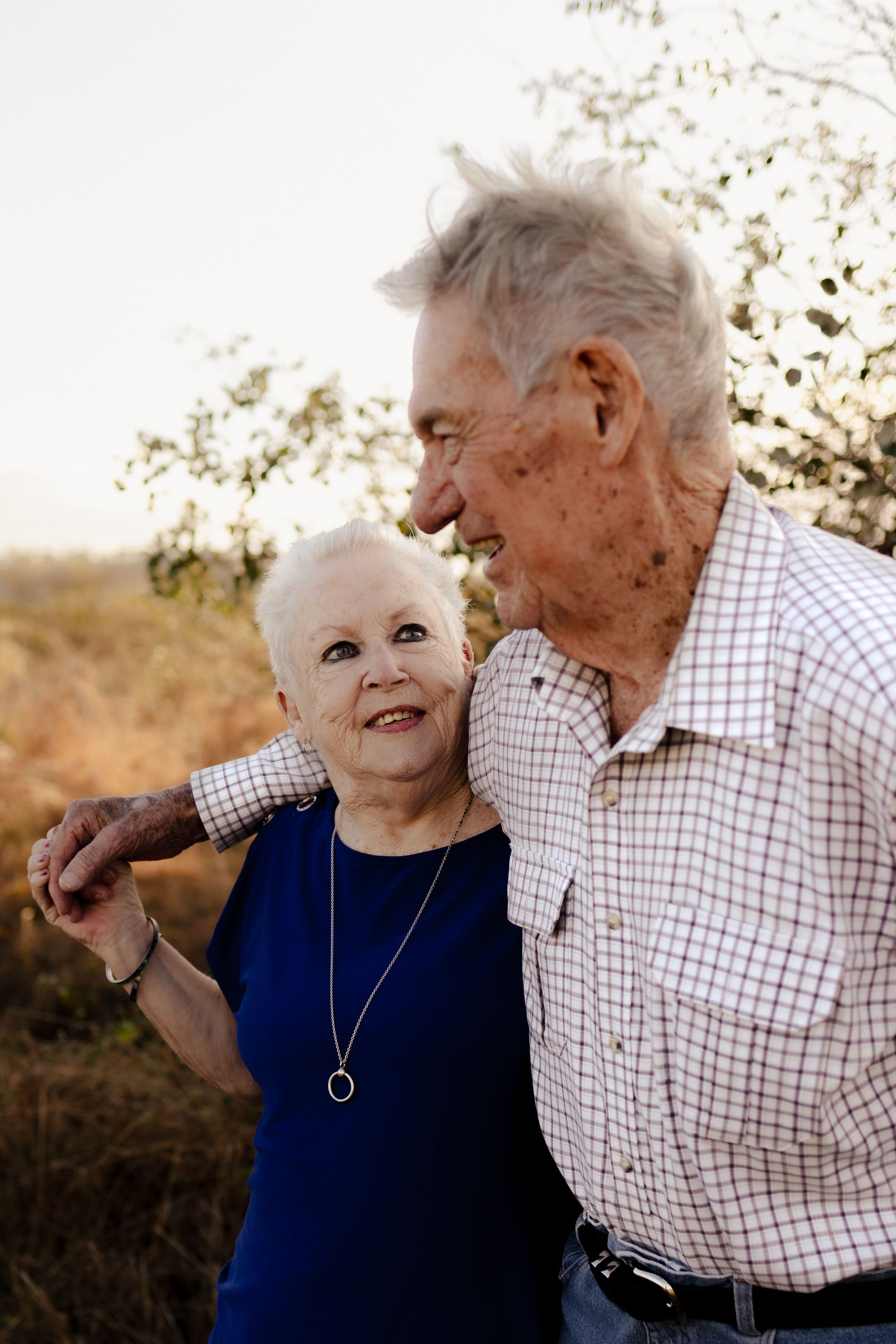 Senior couple laughing together outdoors with sunlit foliage in background.