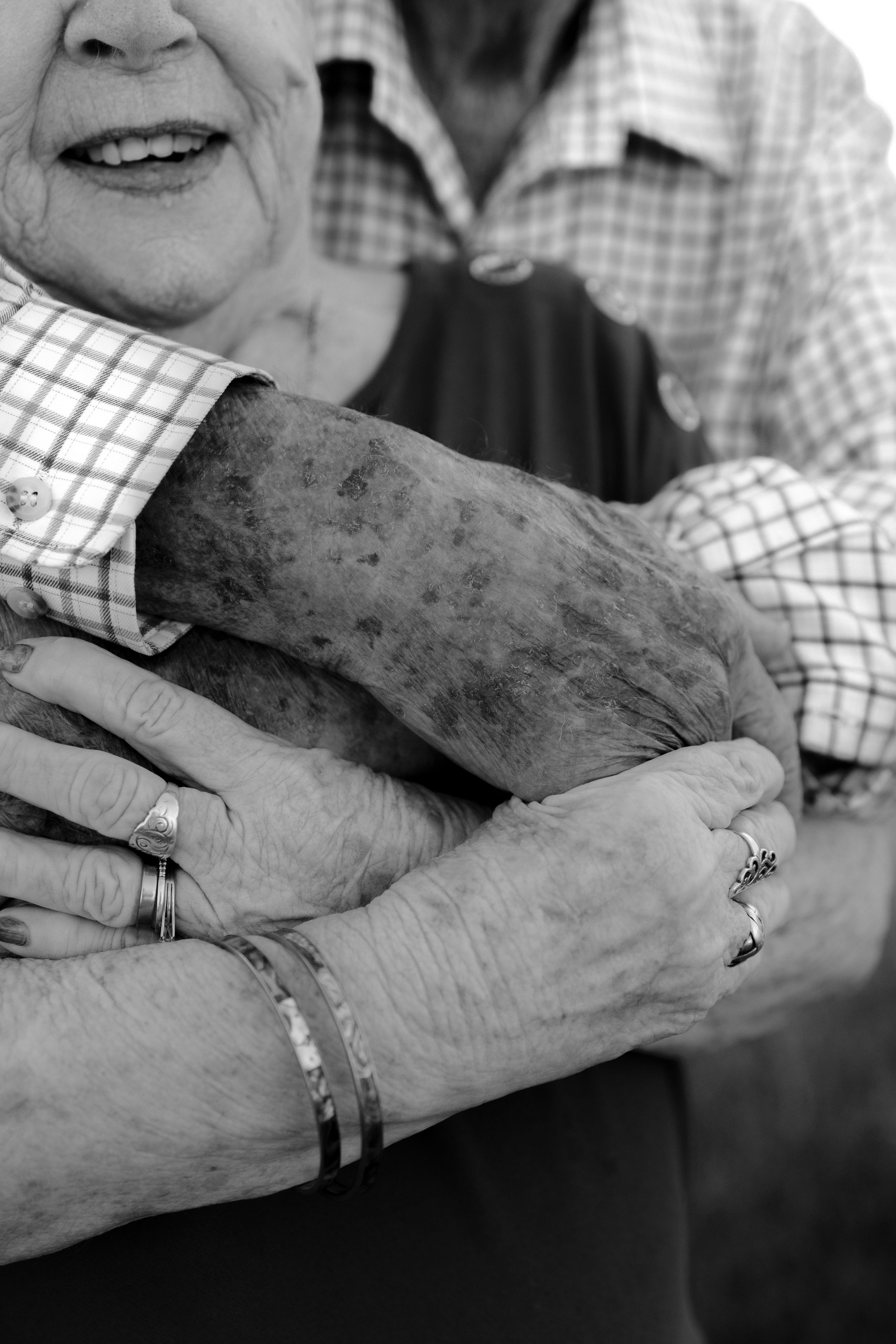 Black and white close-up of elderly couple's hands with wedding rings showing years of love.