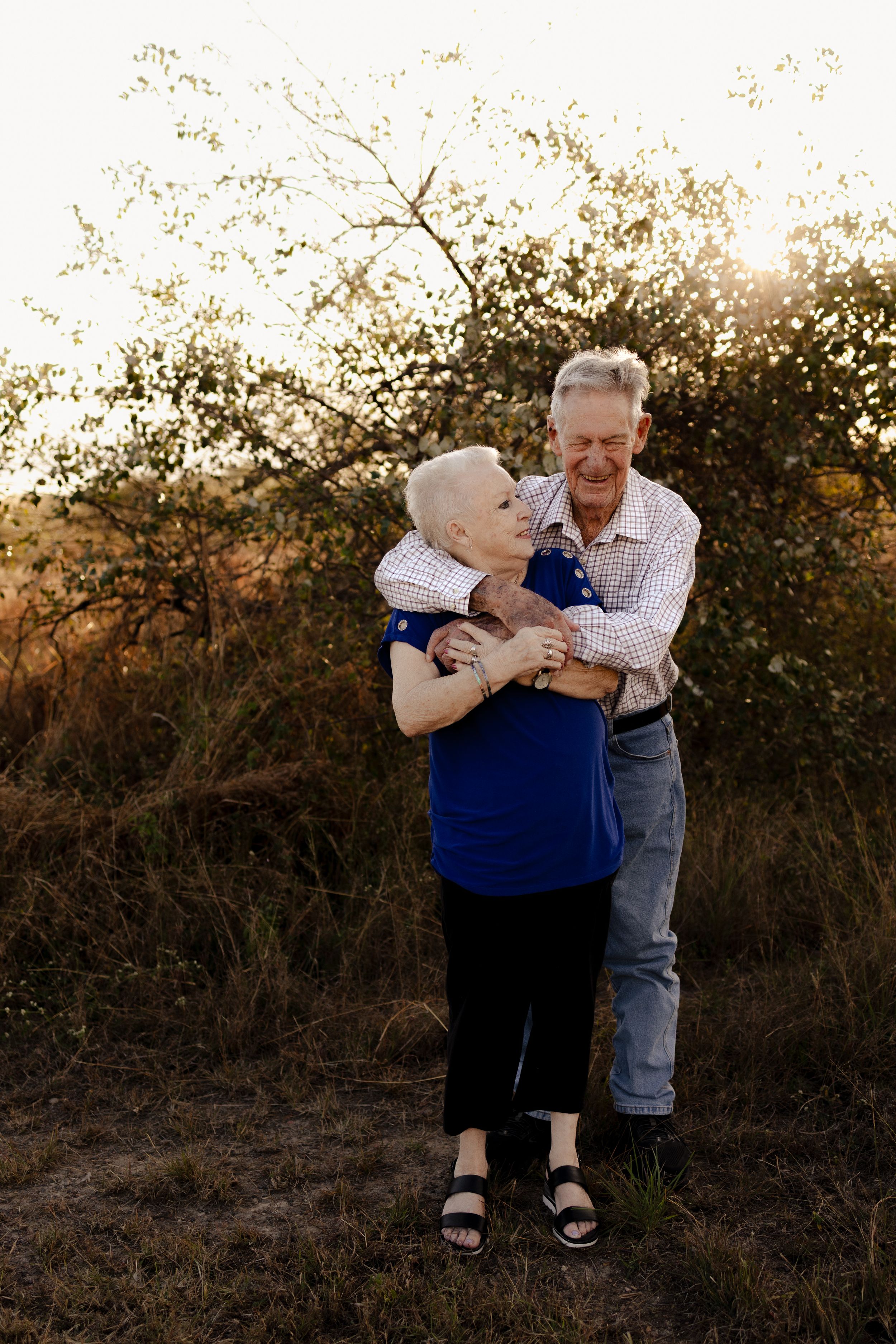 Elderly couple embracing playfully in outdoor setting during sunset.