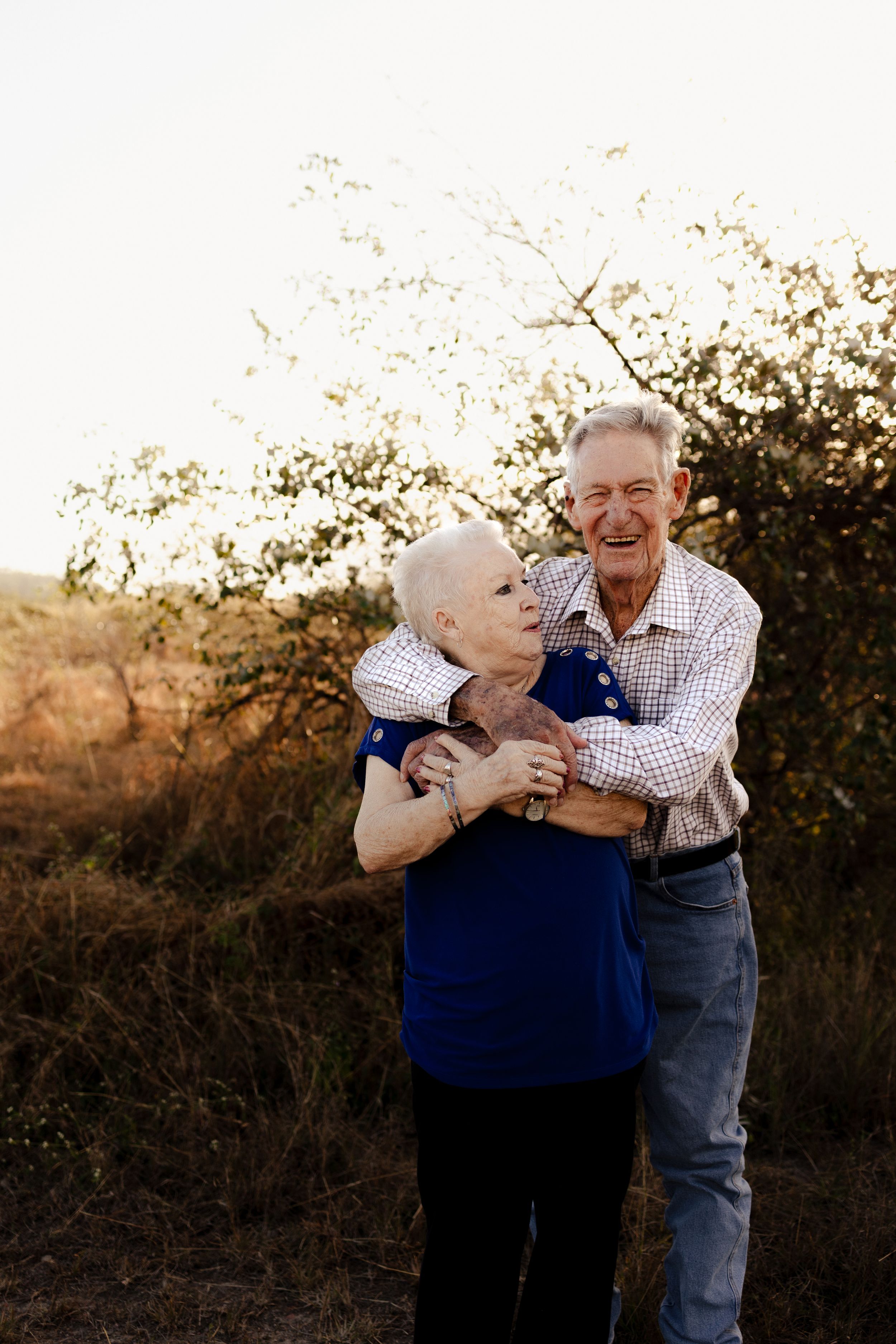Candid moment of elderly couple laughing and embracing in natural setting.