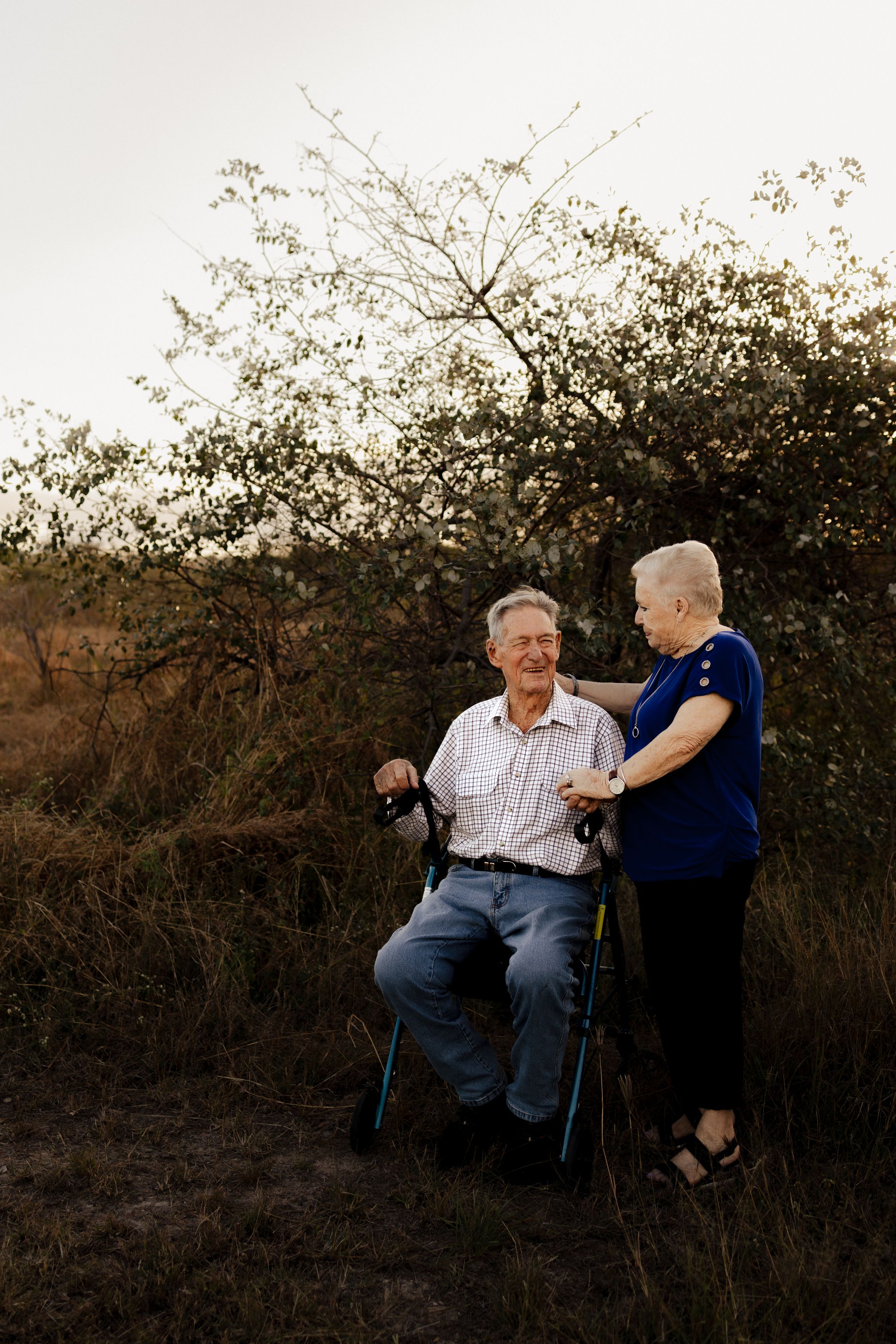 Two people share a tender moment at sunset against a backdrop of silhouetted bushes.