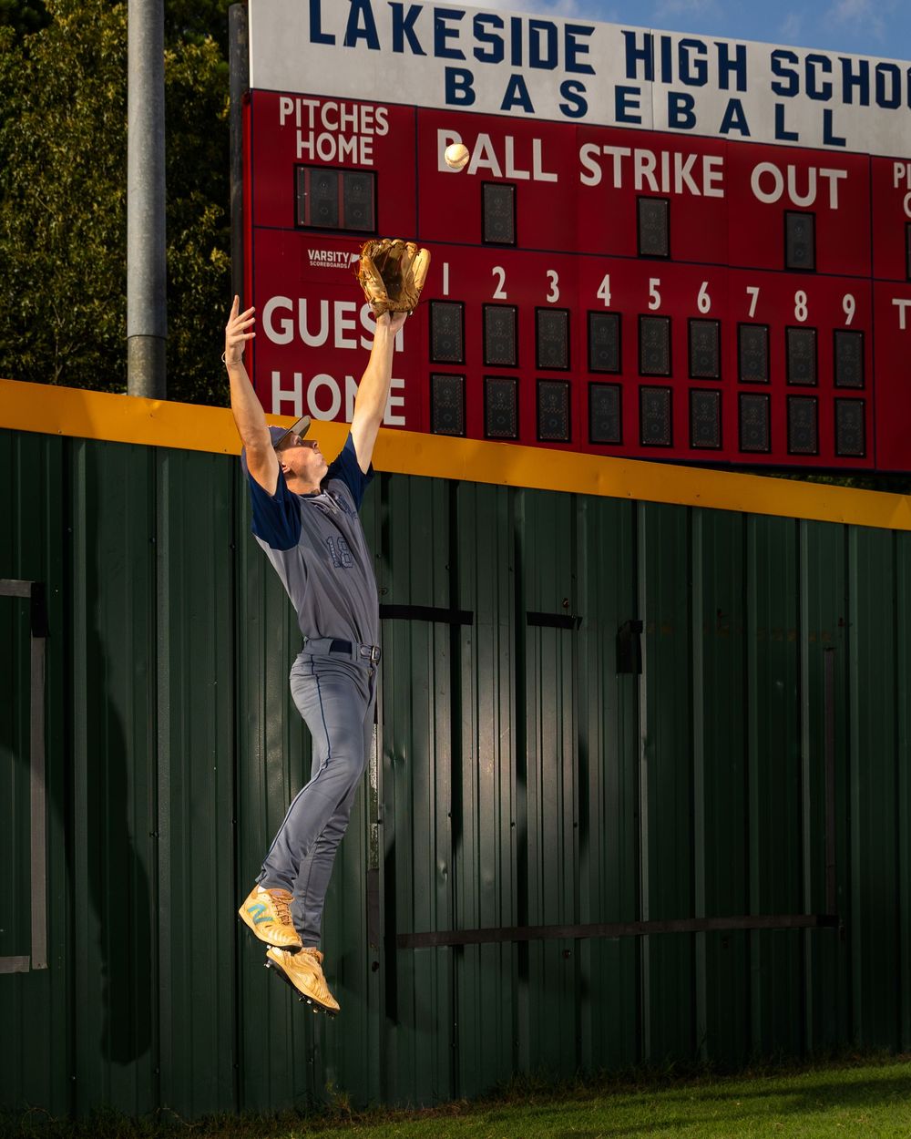 Baseball player makes spectacular leaping catch against scoreboard at Lakeside High School field during game.