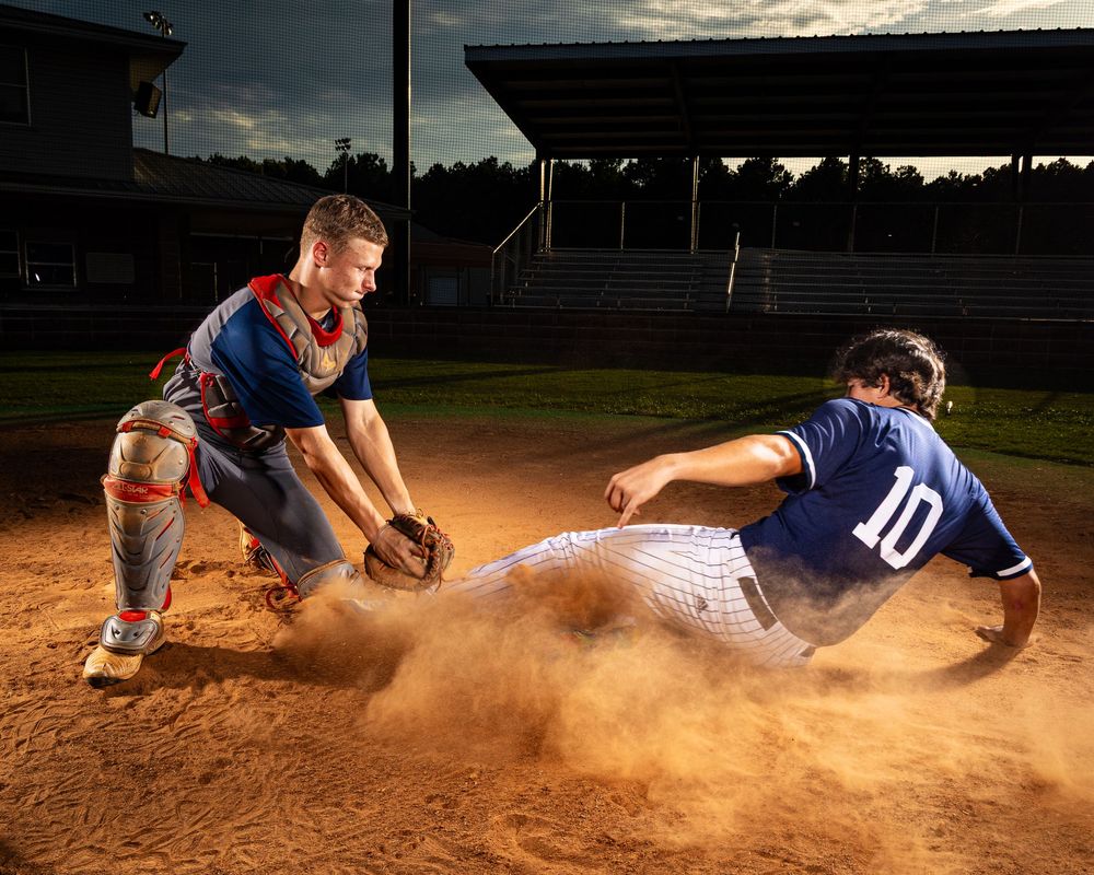 Players dive into home plate creating a cloud of dust during an intense baseball game play.