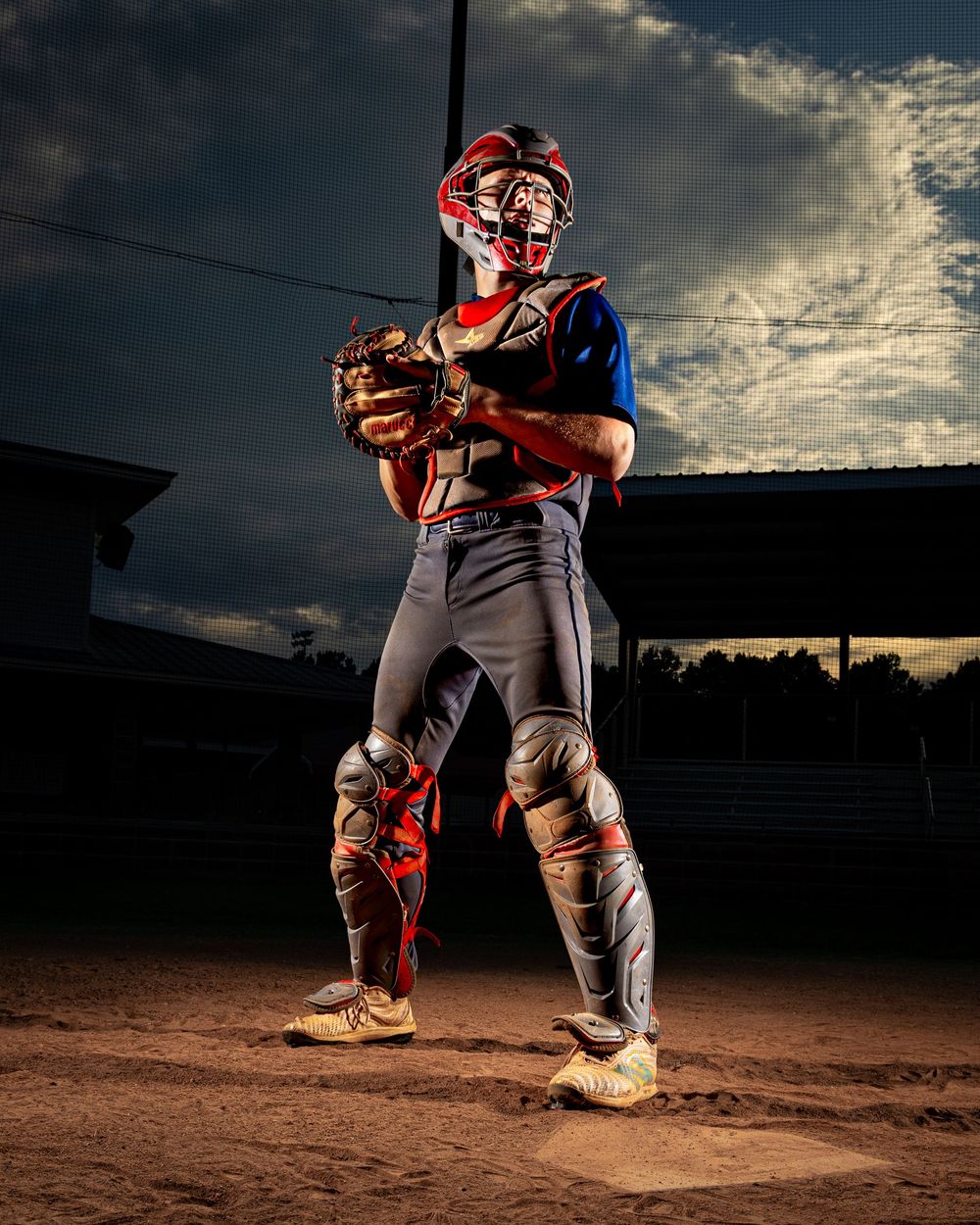 Baseball players on a dirt field at sunset create dramatic silhouettes against a dark cloudy sky.