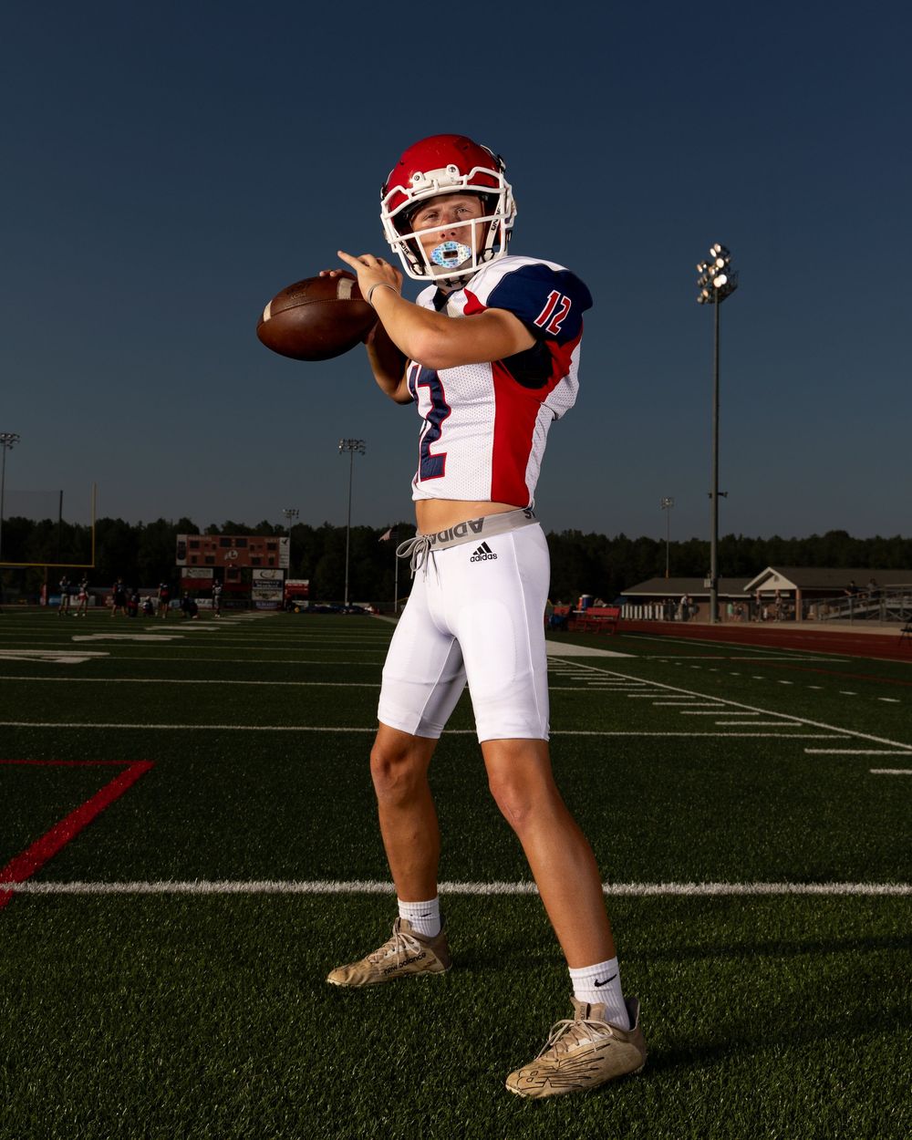 A quarterback in white and red uniform stands ready in throwing position on a football field during practice.
