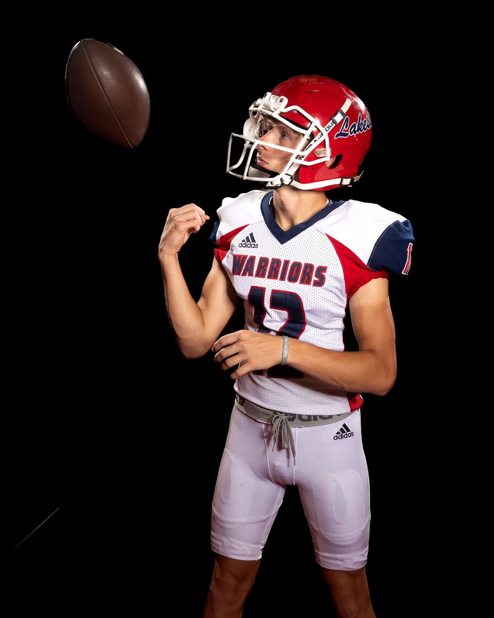 Football player in red and white uniform poses with ball in dramatic black background studio photo shoot.