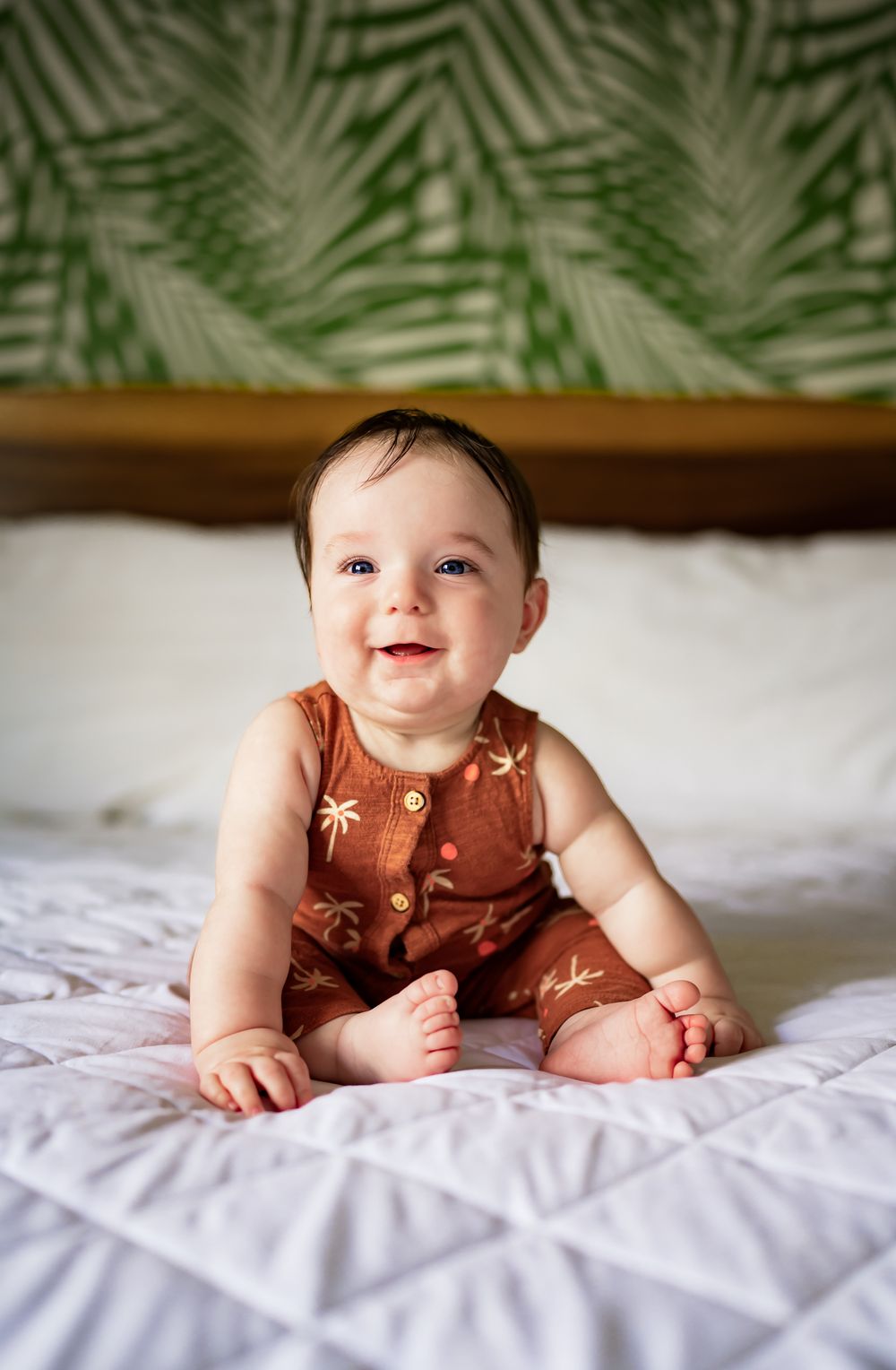 A baby wearing a rust-colored sleeveless romper lies on white bedding while smiling and moving, shown in a series of photos.