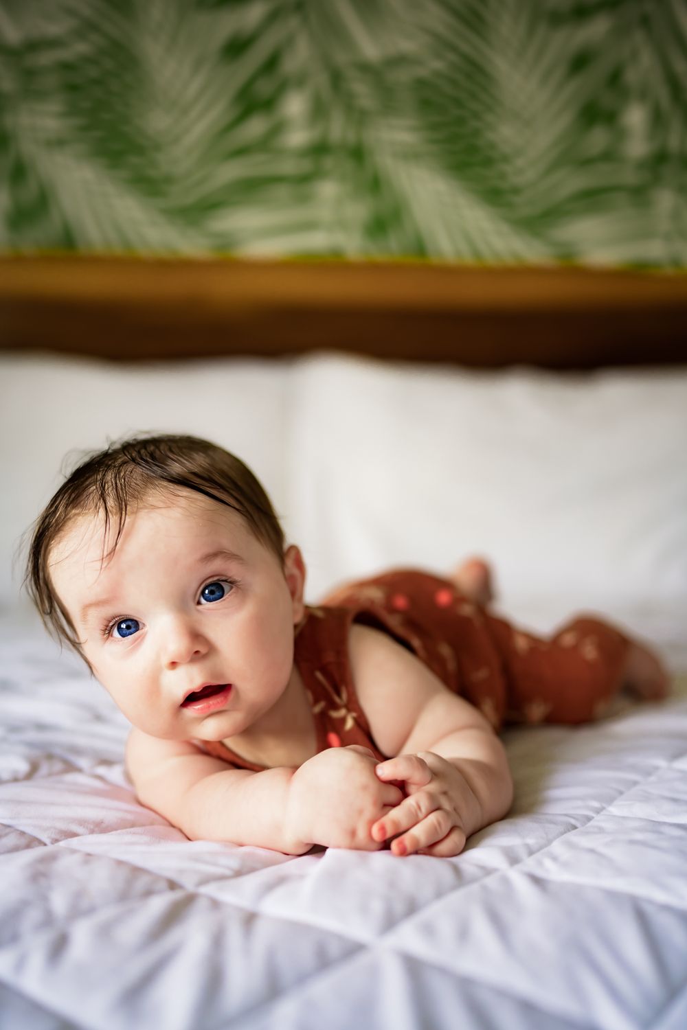 Baby resting on white bedding with palm fronds visible in background decor.