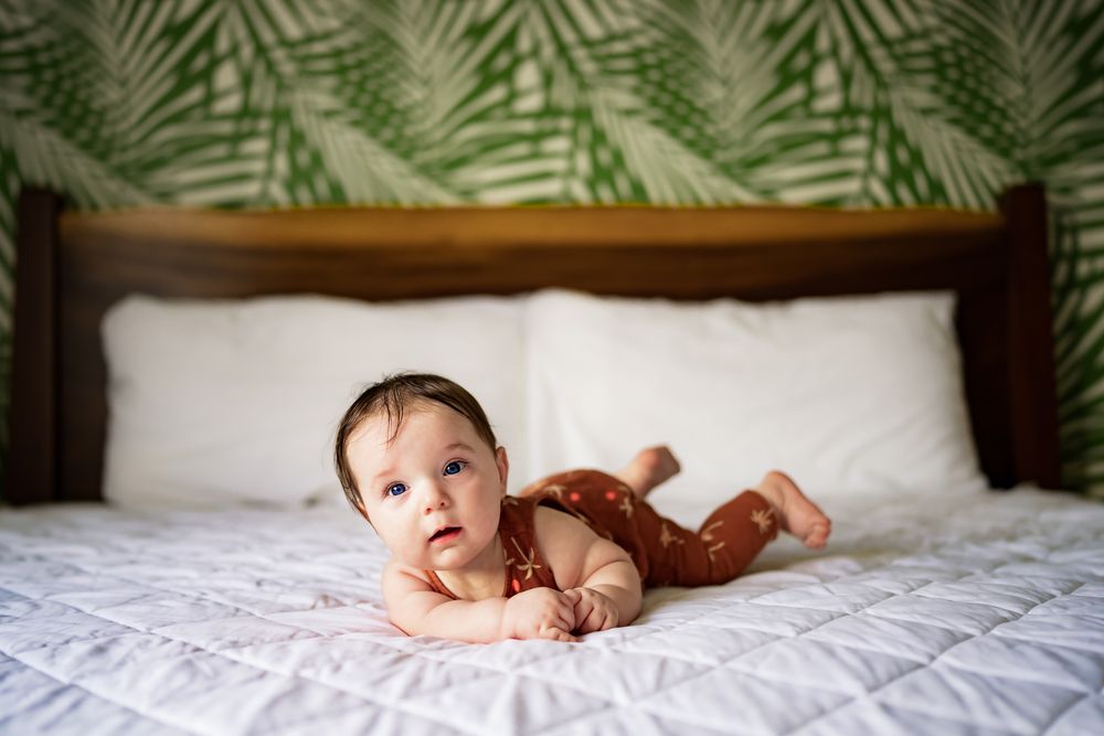 Baby laying on plush white bedding with tropical leaf wallpaper backdrop.