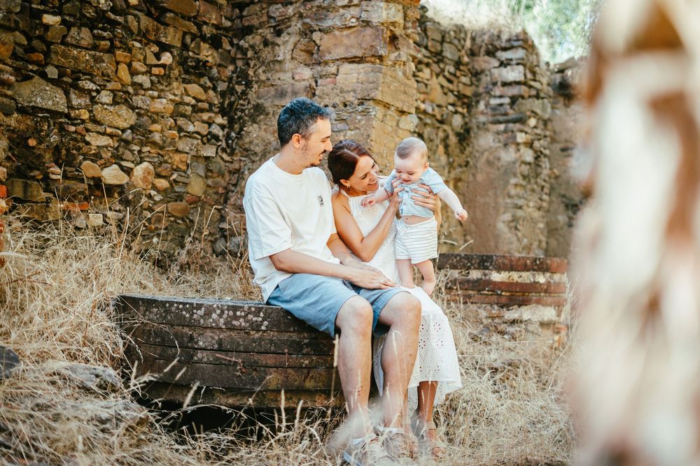 A loving family with a baby sits in a vintage wooden boat surrounded by golden hay and stone walls.