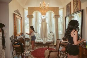 Elegant sunlit room with chandelier, wicker furniture and floor-length drapes creating a warm, inviting interior space.