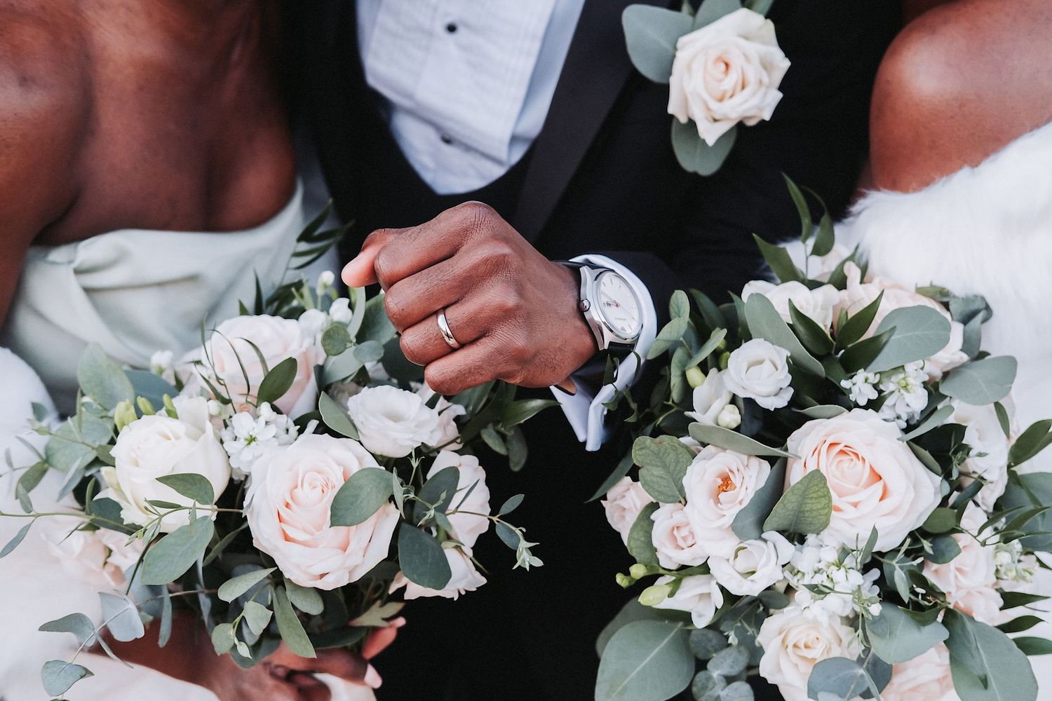 Delicate white and blush wedding bouquet featuring roses and greenery against dark background.