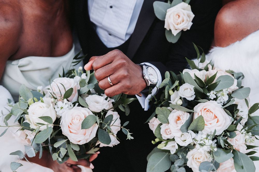 Delicate white and blush wedding bouquet featuring roses and greenery against dark background.