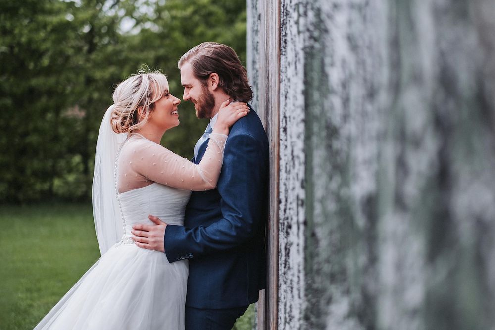 Two people in wedding attire embrace in front of a rustic barn door.