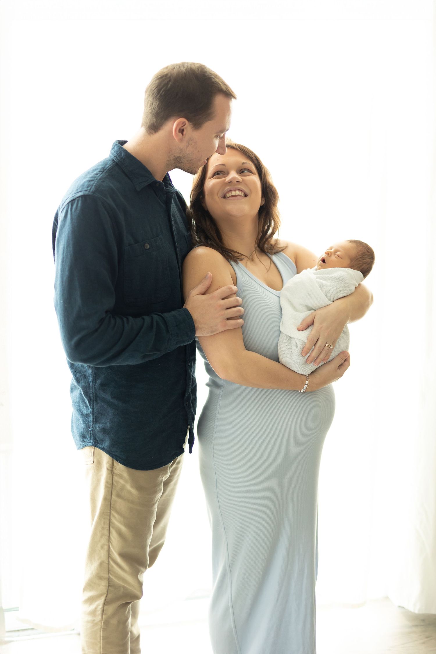 New parents smiling at each other while holding their newborn