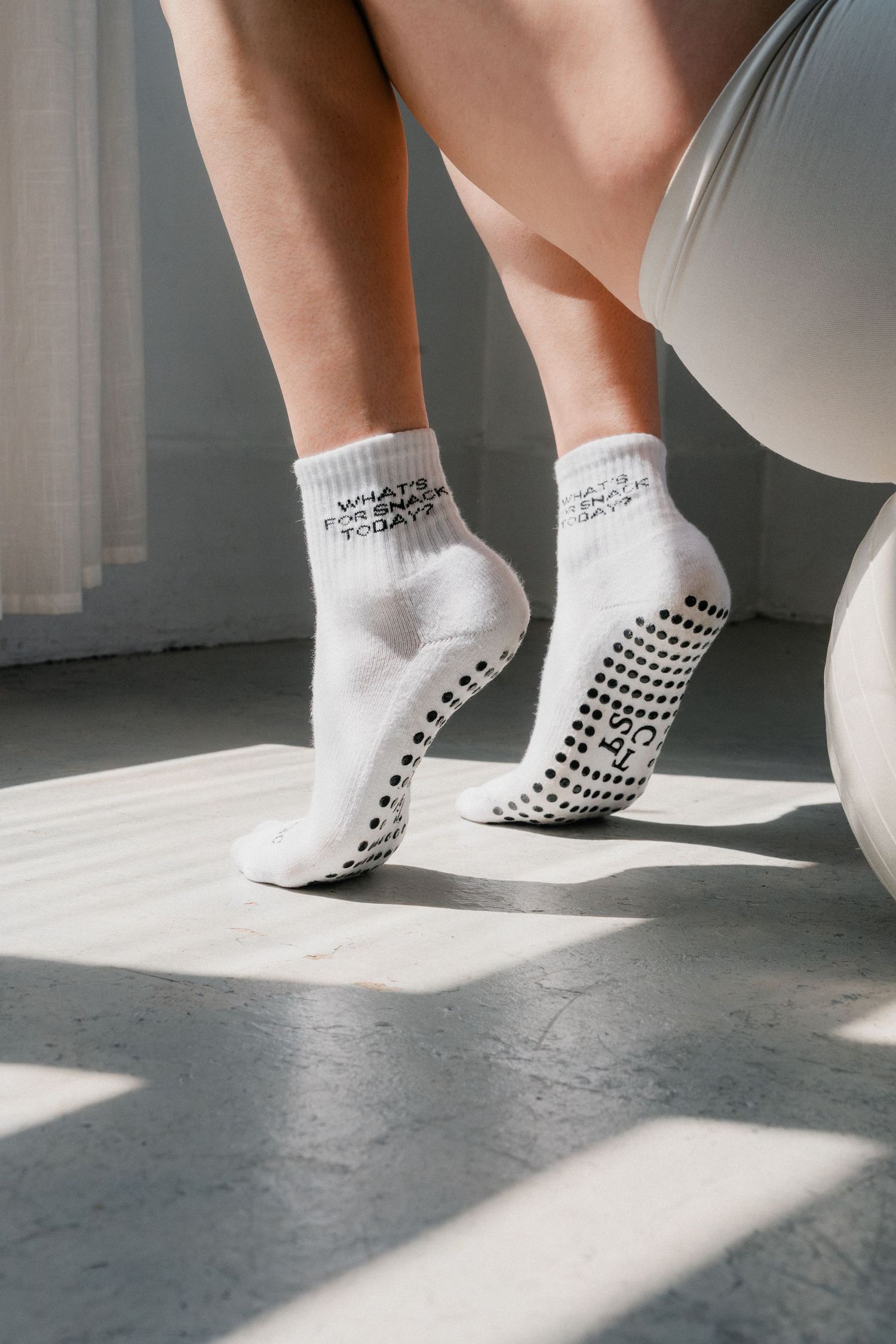 White grip socks with black non-slip dots cast shadows on a light gray floor in various walking positions.