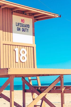 A series of wooden lifeguard towers numbered 16-18 with 'No Lifeguard On Duty' signs on a sunny beach.