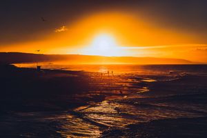 Dramatic orange and yellow sunset silhouettes over calm ocean waters with vibrant sky reflections.