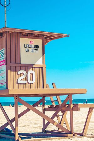 Lifeguard station numbered 20 with warning signs on beach under clear blue skies.
