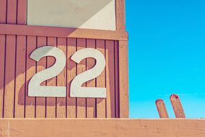Row of numbered brown wooden lifeguard station towers against bright blue sky on empty beach.