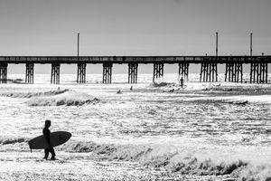 Five black and white surfing scenes showing surfers riding waves near a pier in dramatic winter surf conditions.