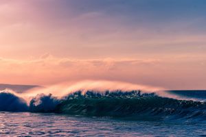 Rolling ocean waves crash at sunset creating a dynamic seascape with pink and purple hues.