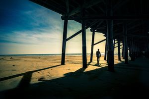 Oceanside pier silhouetted against a vibrant orange sunset sky with the ocean reflecting the warm light.
