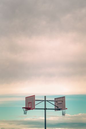 Double basketball hoops silhouetted against pastel sky with soft clouds creating symmetrical sports composition.