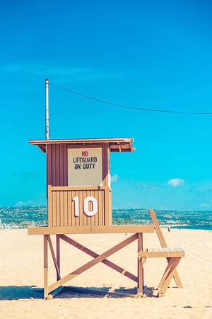A series of beige wooden lifeguard towers with number 10 marking on a sunny beach against bright blue sky.