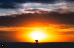 Dark storm clouds hover over the horizon during a vivid orange coastal sunset.