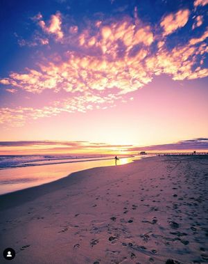 Panoramic sequence of a dramatic purple and orange sunset over a serene beach with footprints in the sand.