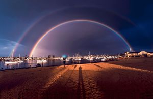 Long shadows cast on beach sand at night with city lights glowing along the distant coastline.