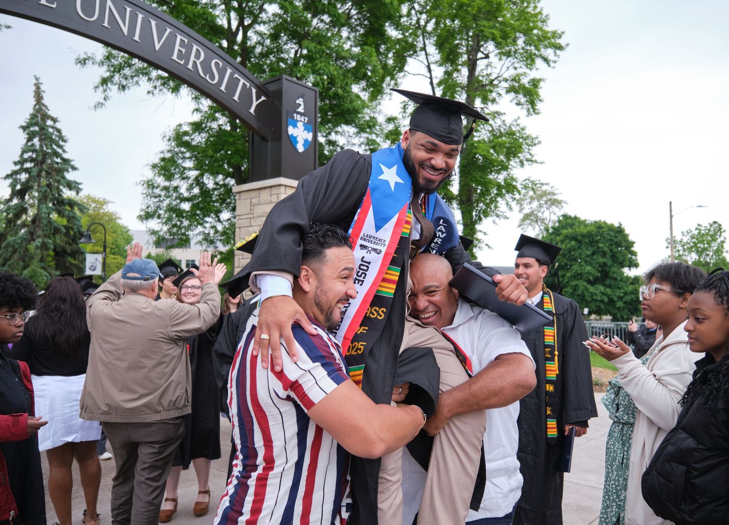 A commencement photo of a graduate being lifter by family members after the ceremony.
