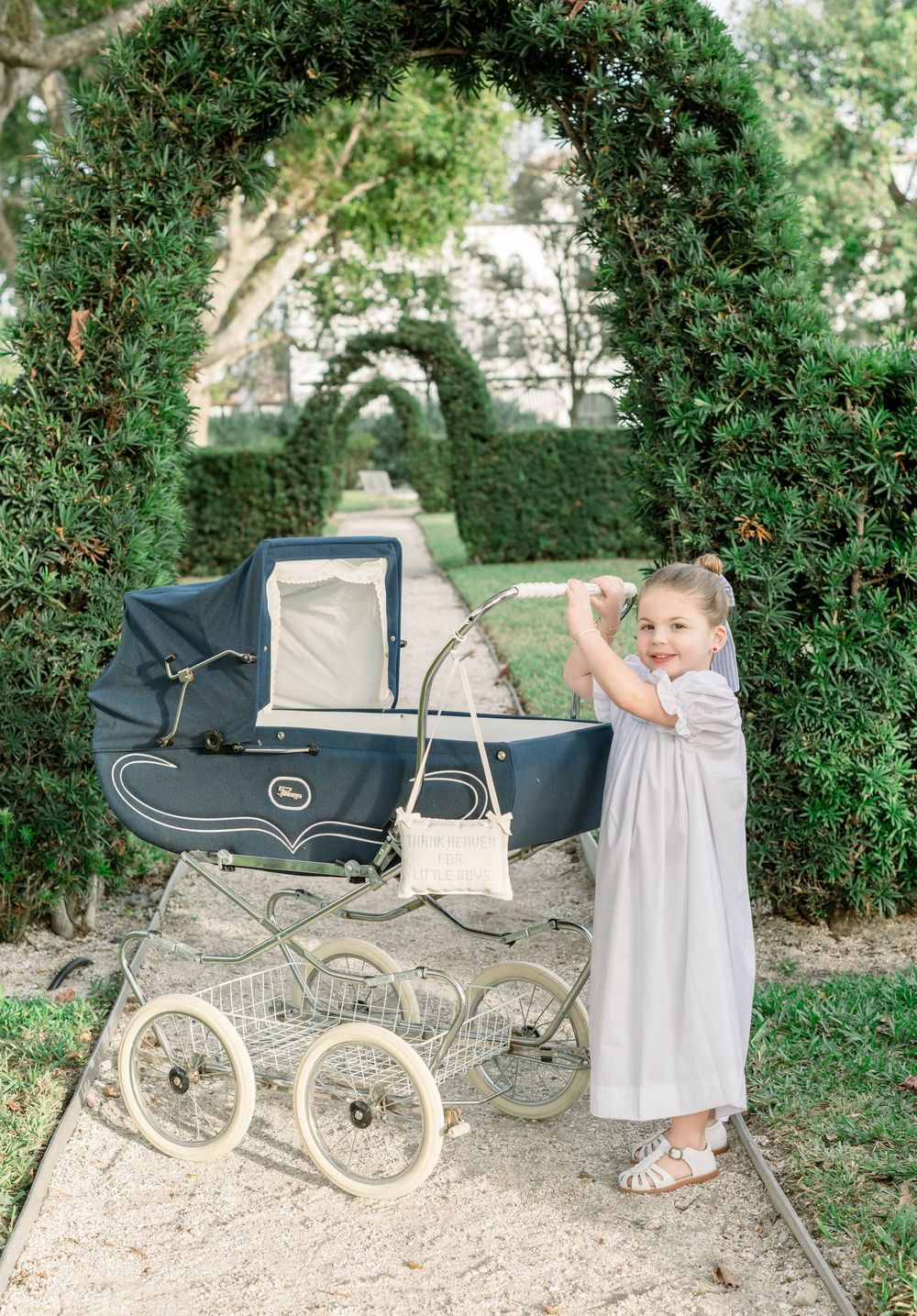 Vintage navy blue baby carriage on garden path with child in white dress.
