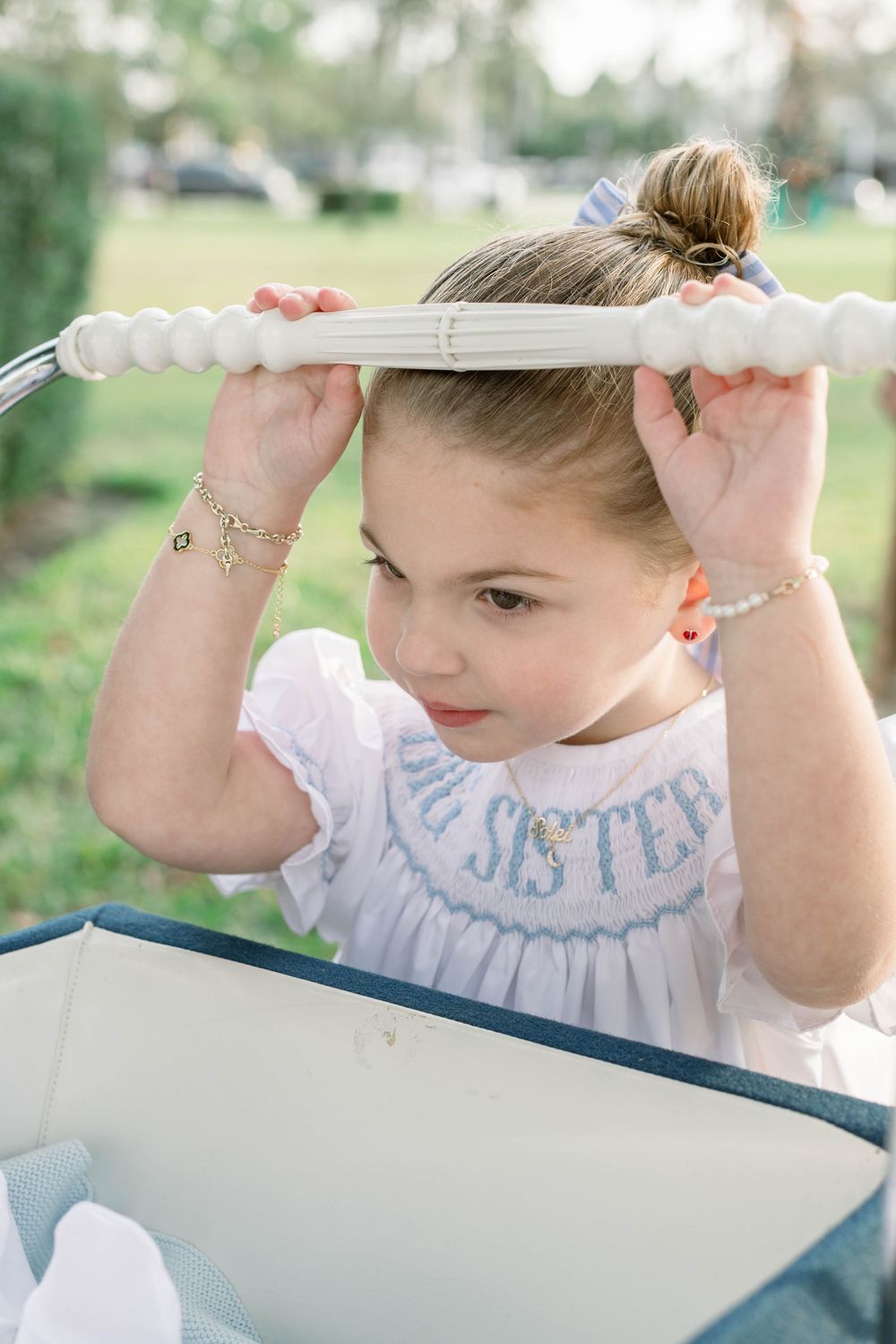 Child wearing white embroidered dress with blue details in outdoor setting.