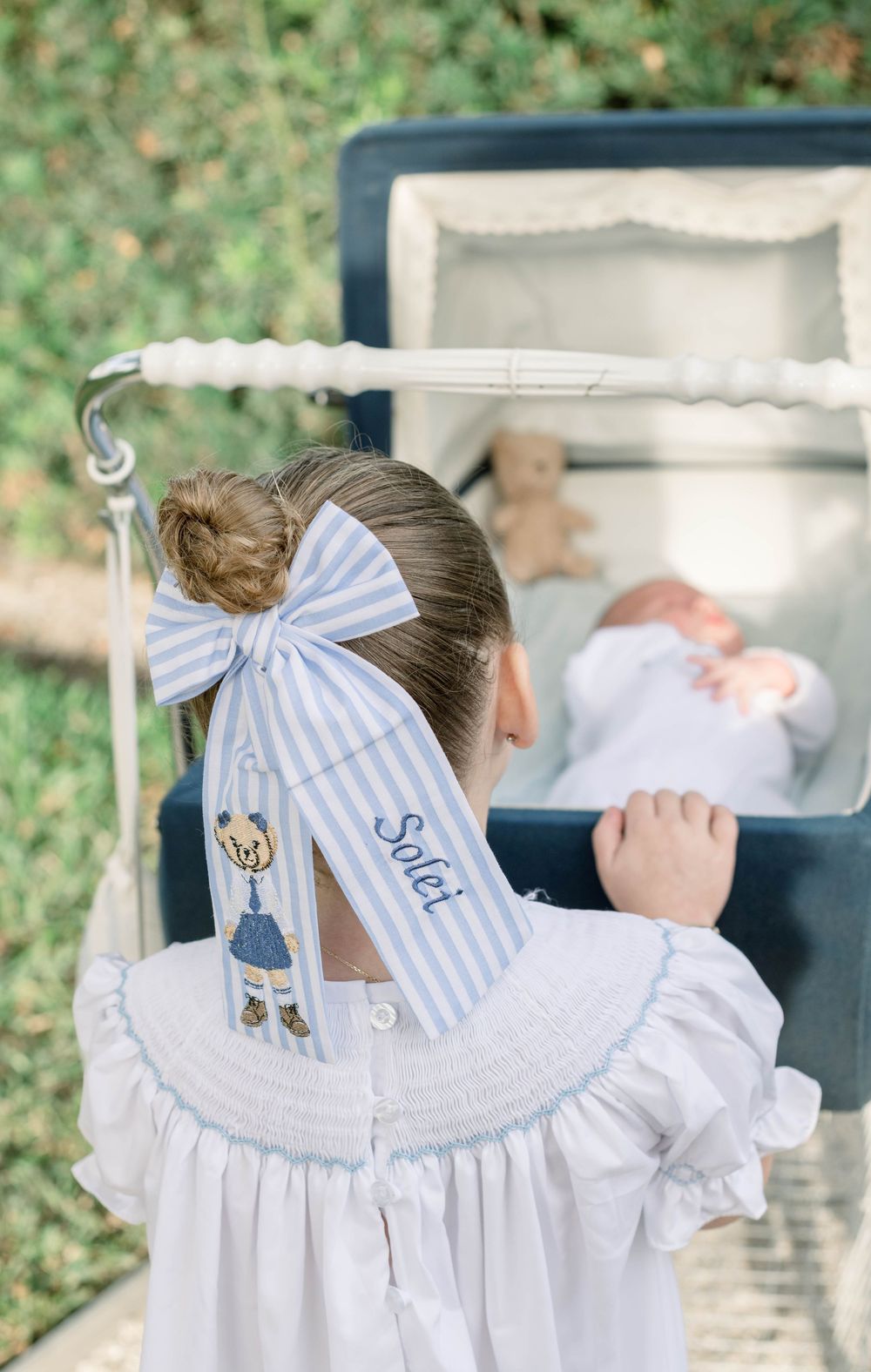 White dress with blue striped bow and embroidered teddy bear details.