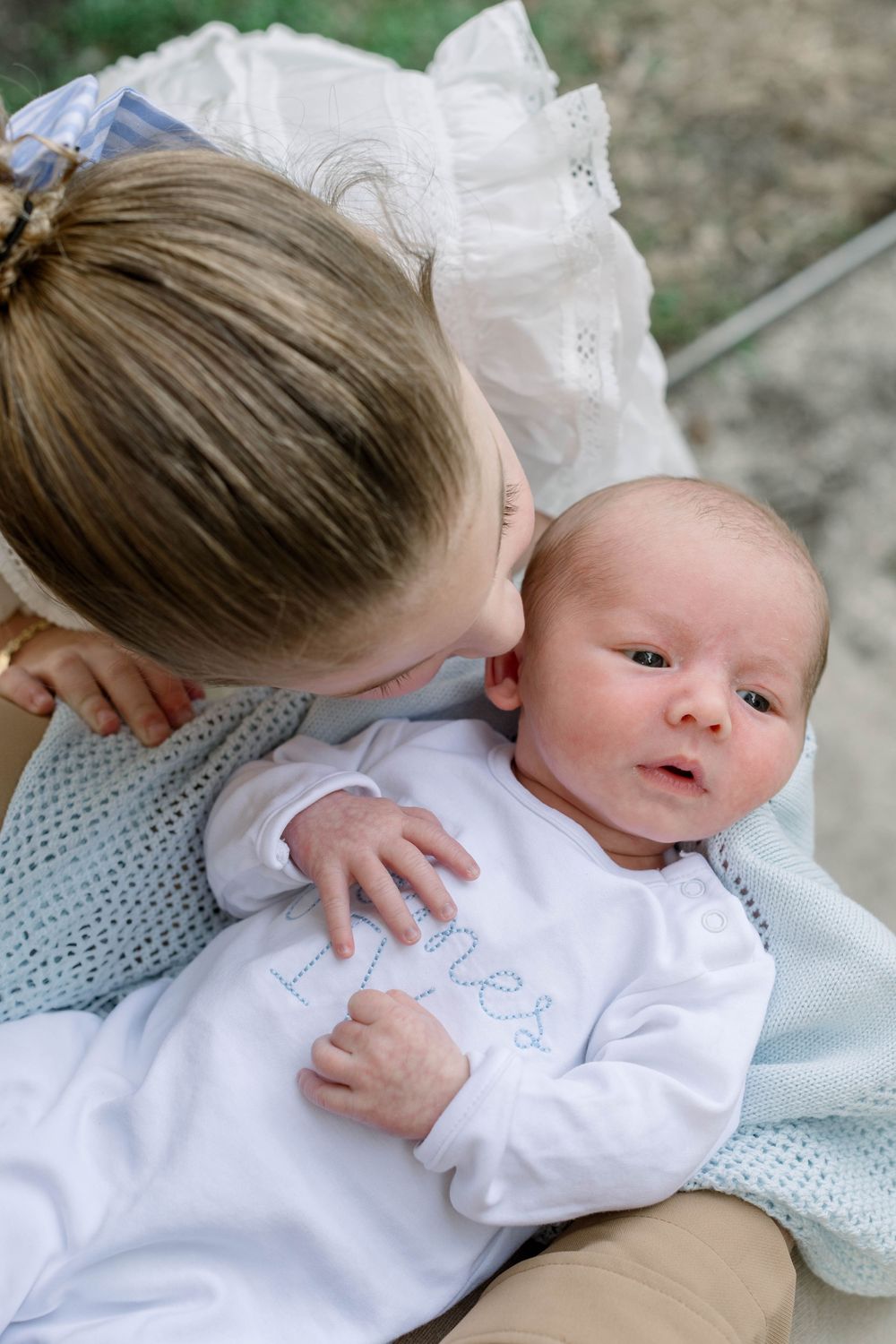 Tender moment with baby in white outfit resting on knitted blanket.