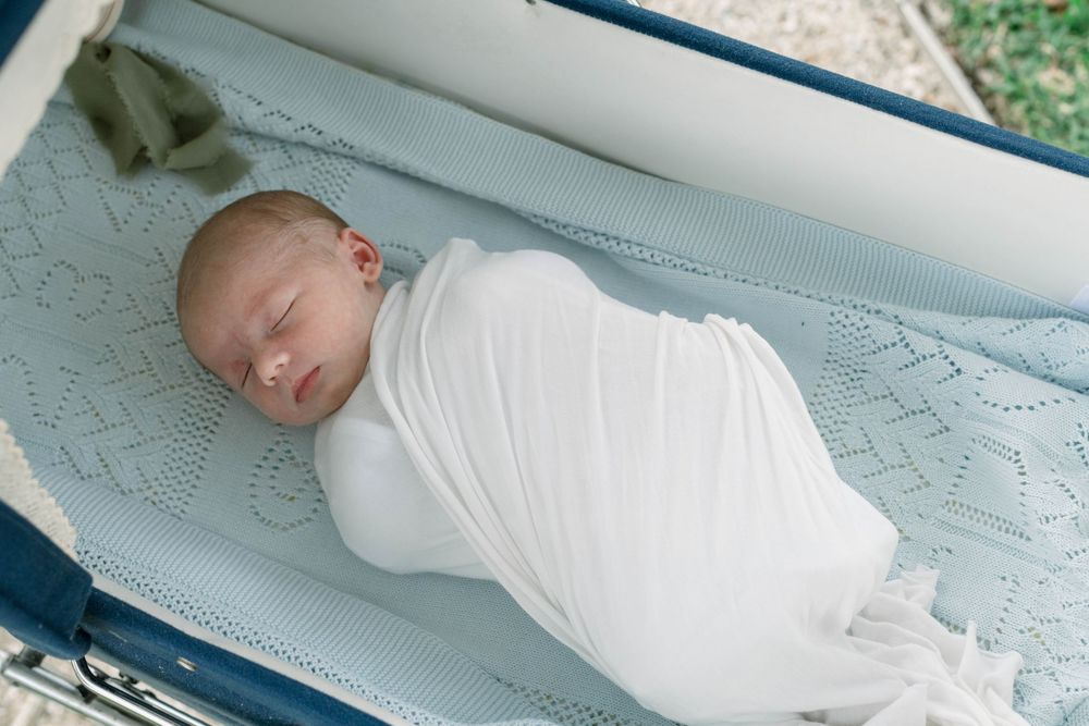 Baby sleeping peacefully in white clothing on light blue surface.