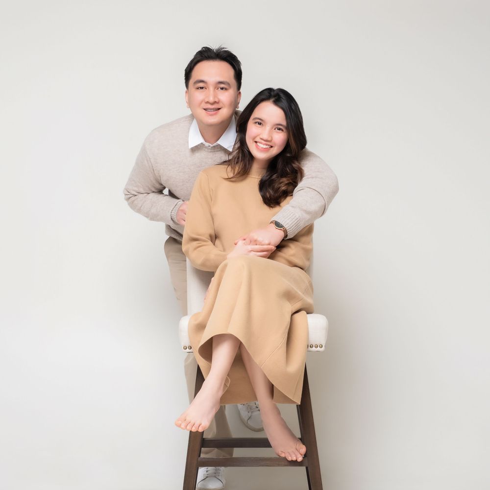 A couple in light-colored outfits poses playfully in front of a white background during a studio photoshoot session.