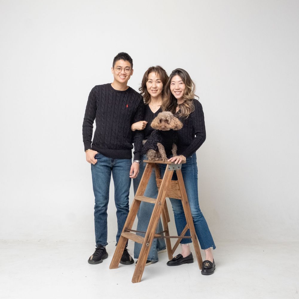 People sitting on wooden stepladder with their goldendoodle puppy in white studio setting.