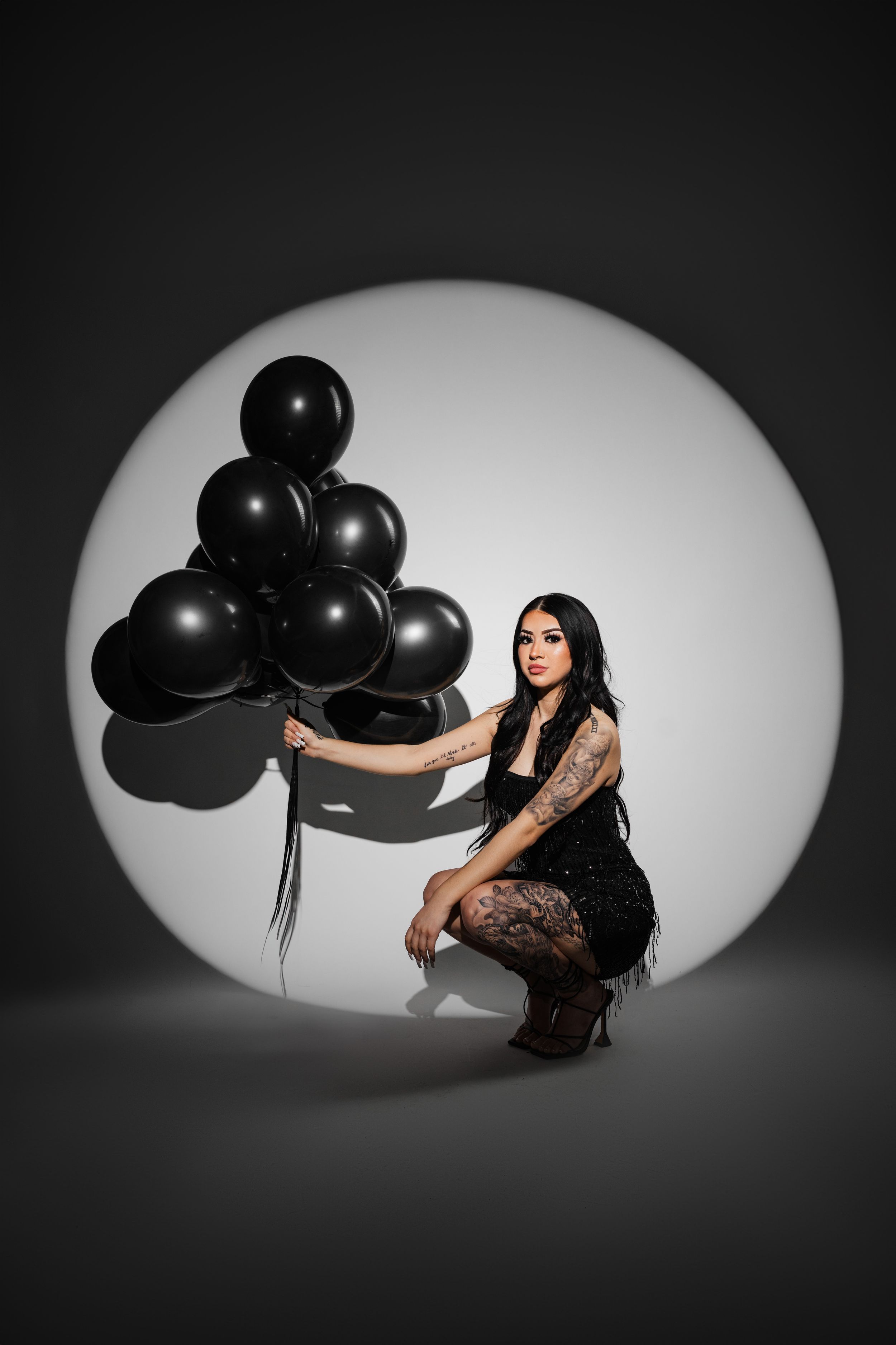 Artistic photo series showing a figure posing with black balloons against a dramatic white oval backdrop.