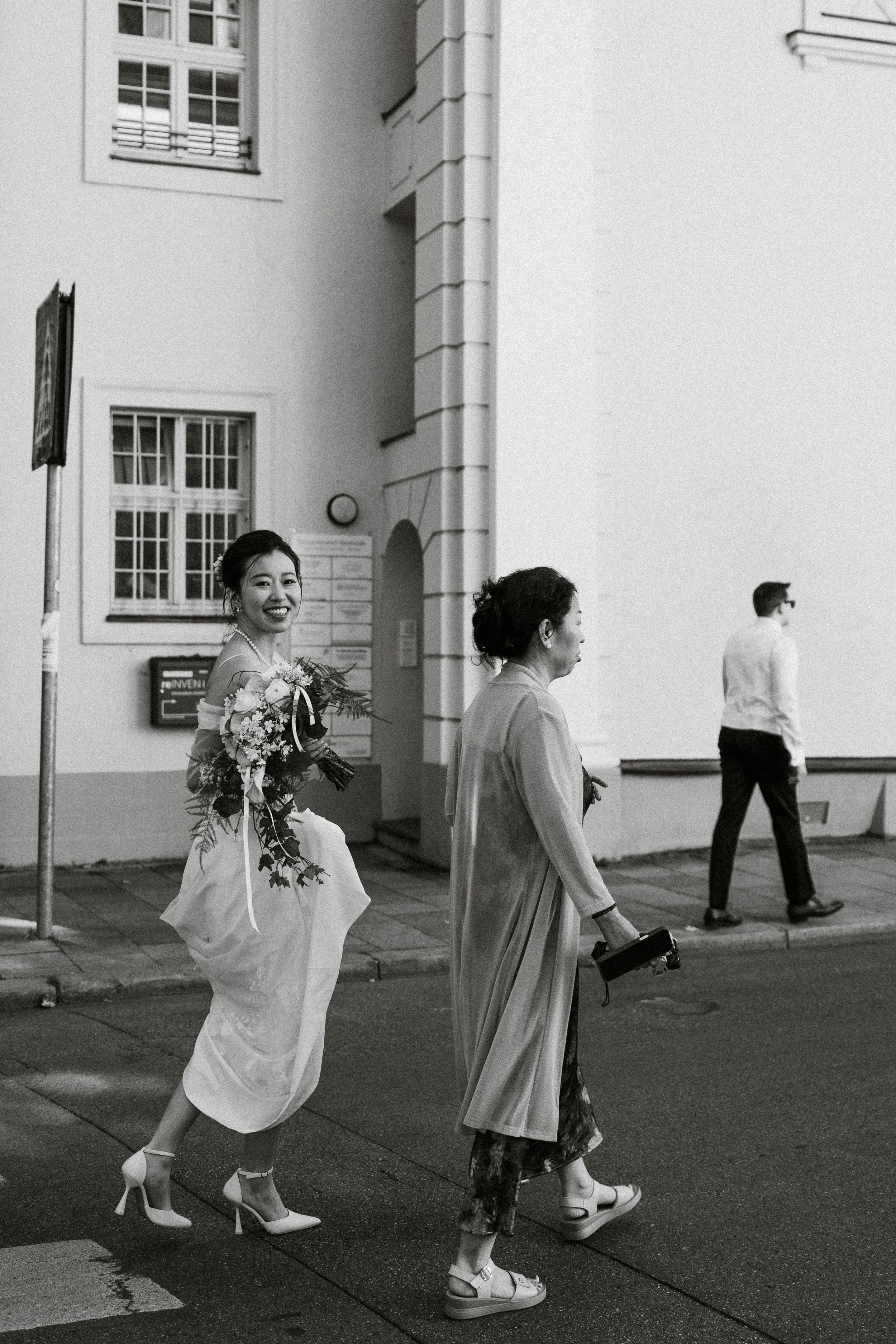 Black and white photo of people walking past white building facade.