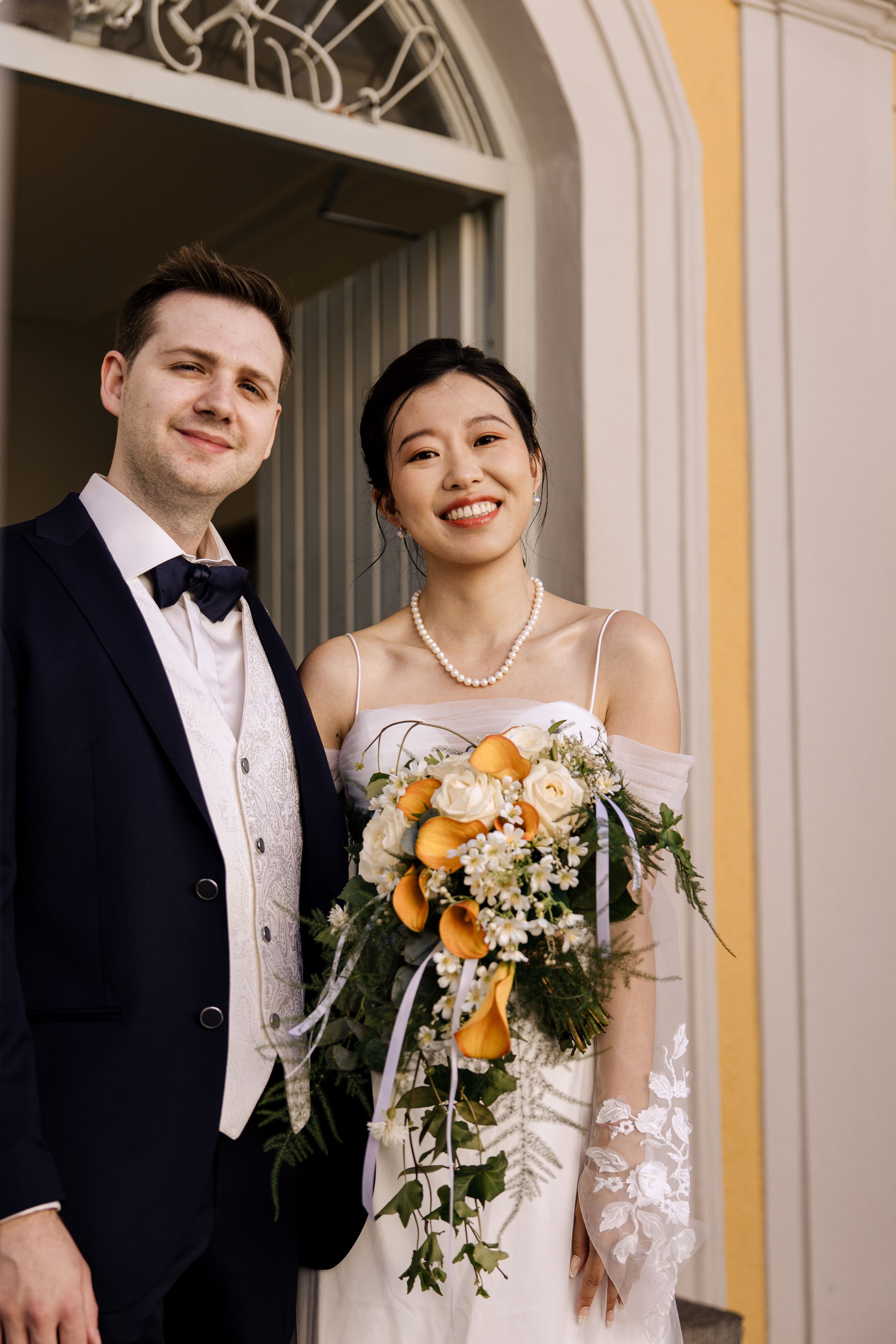 Wedding portraits under beautiful archways with bride holding orange and white floral bouquet.
