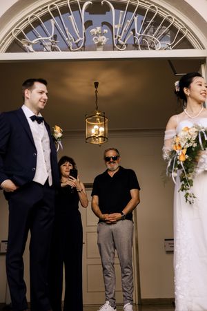 Wedding party gathering under ornate archway with decorative ceiling details.